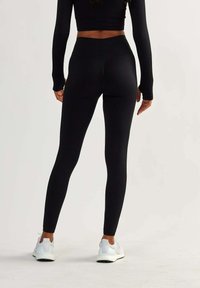 Black high-waisted leggings made of textured fabric, featuring a fitted design, seamless finish, and a smooth waistband. Paired with white sneakers.
