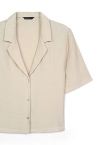 Blusa beige a maniche corte con colletto a revers e tre bottoni sul davanti, in tessuto leggero e testurizzato.