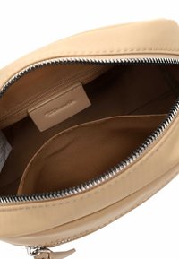 Beige Reißverschlusstasche, geöffnet, um das braune Stoffinnere mit einer kleinen Innentasche und einem eingenähten Markenlabel im Inneren zu zeigen.