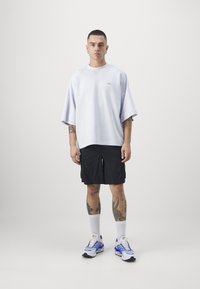 Løs mage lett lilla t-skjorte med korte ermer, kombinert med svarte shorts. Utseendet fullføres med hvite sokker og flerfargede joggesko.
