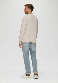 Helles beiges Sweatshirt mit gerippten Bündchen, kombiniert mit hellblauen Denim-Jeans. Das Modell trägt weiße Sneaker. Von hinten vor einem schlichten Hintergrund zu sehen.