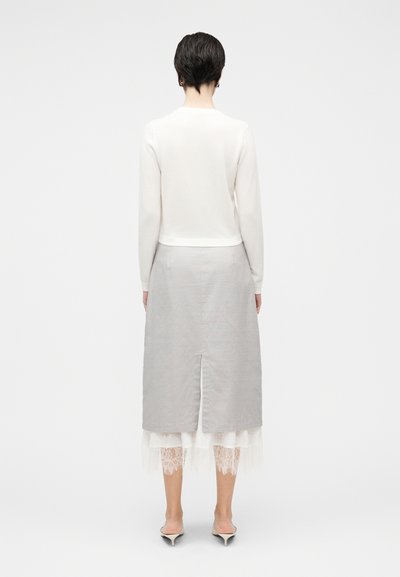 Bela majica z dolgimi rokavi v kombinaciji z sivo krilo. Krilo ima zarezo na sredini zadnjega dela in večplastno belo čipkasto obrobo na robu.