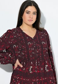 Kleid mit tiefem V-Ausschnitt in Dunkelrot, mit einem gemischten Muster aus weißen und hellroten Akzenten. Verfügt über lange, gepuffte Ärmel und strukturierte Stoffoberfläche.