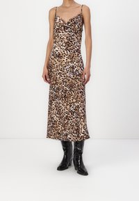 Robe longue en satin à imprimé léopard avec un col bénitier et des fines bretelles ; associée à des bottines à talons noires pour le contraste et la texture.