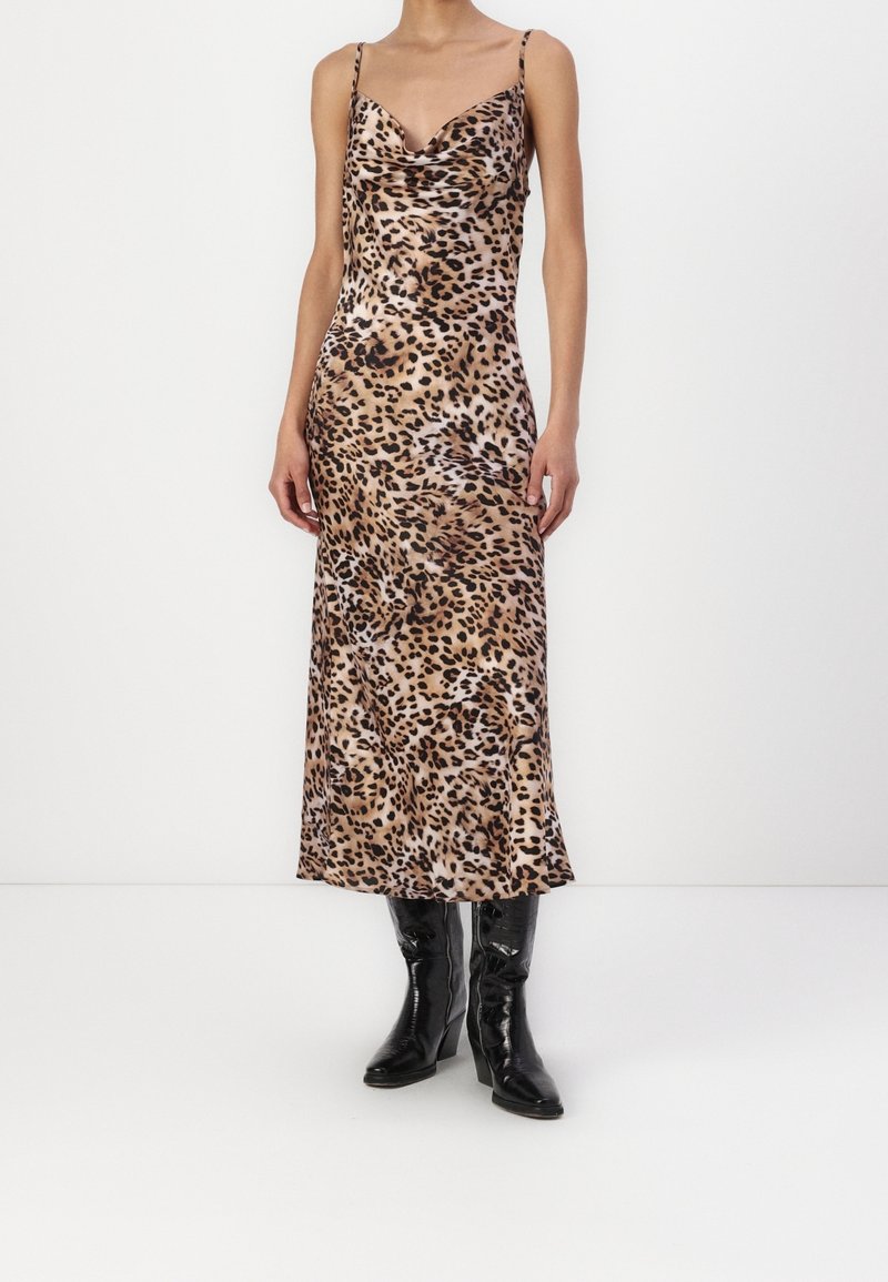 Robe longue en satin à imprimé léopard avec un col bénitier et des fines bretelles ; associée à des bottines à talons noires pour le contraste et la texture.