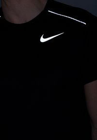 Černé sportovní tričko s reflexními detaily na ramenech a výrazným bílým logem Nike na hrudi.