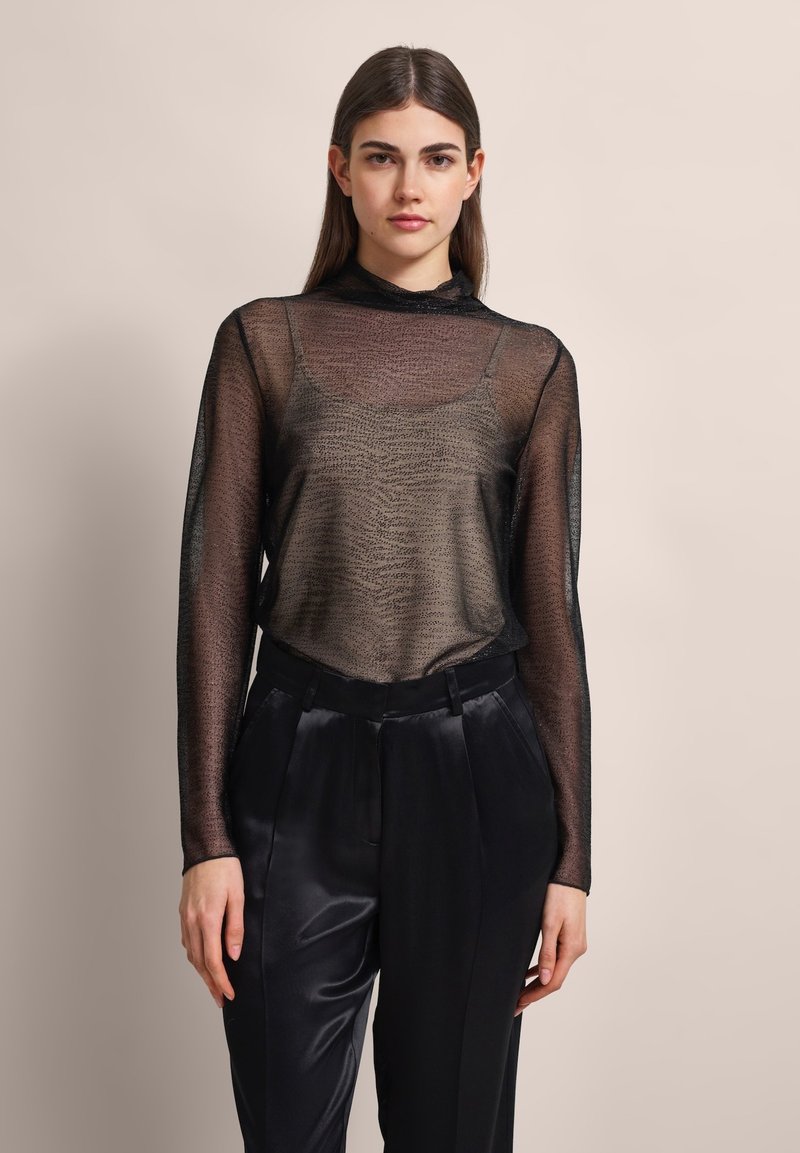 Schwarzes, transparentes Langarmoberteil mit einem strukturierten Muster, kombiniert mit einer hochtaillierten schwarzen Satin-Hose. Glattes Gewebe mit leichtem Glanz.