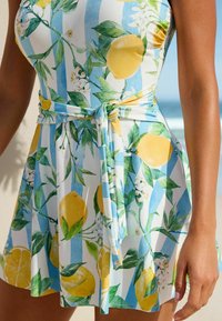Blumenkleid mit gelben Zitronen und grünen Blättern auf einem weiß-blauen gestreiften Hintergrund. Weicher Stoff mit einem gebundenen Taillendetail.
