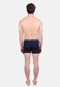 Shorts de bain navy avec imprimé ours orange, dotés d'une ceinture blanche avec logo. Fabriqués en tissu doux, conçus pour le confort et l'ajustement.