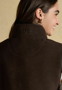 Brauner Fleece-Weste mit hohem Kragen, auf der Rückseite mit "JOULES" geprägt. Weiche Textur; minimales Design ohne sichtbare Verschlüsse.