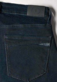 Jeans de mezclilla oscura con un bolsillo trasero prominente, etiqueta de cuero en la cintura y detalles de costura en contraste, que muestran un diseño clásico.