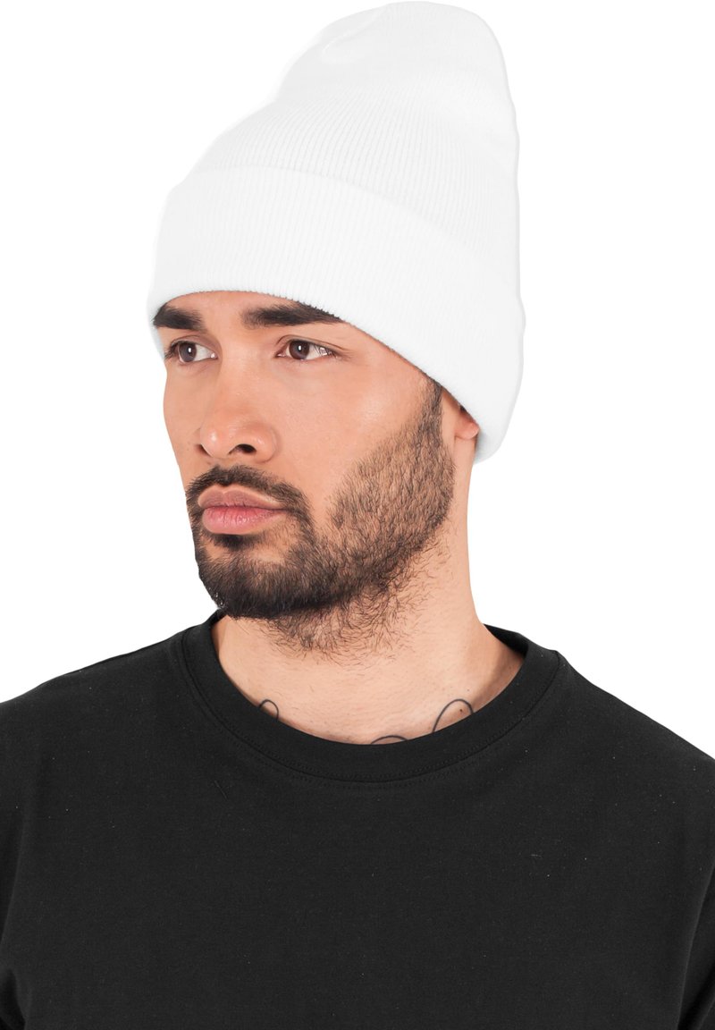 Beanie bianca a maglia con risvolto, caratterizzata da una morbida texture a coste. Indossata da un individuo con una maglietta nera a girocollo, espressione concentrata.