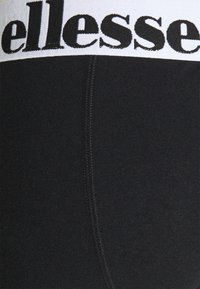 Svarta leggings i en strukturerad tygkvalitet, med en bred vit midjeband prytt med "ellesse" i svarta bokstäver och synliga sömdetaljer.