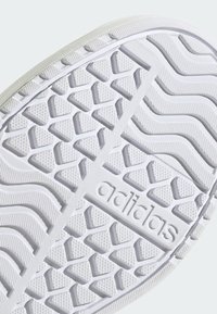 Semelle de sneaker blanche présentant un motif de crampons hexagonal et des textures ondulées, avec le logo "adidas" embossé sur le côté.