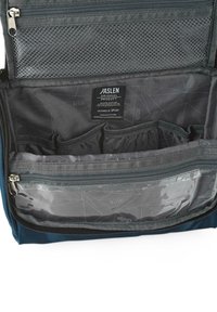 Interior de una bolsa de viaje azul con múltiples compartimentos, un bolsillo de malla con cremallera y una sección transparente. Etiquetada con "JASLEN" y detalles de diseño en gris.
