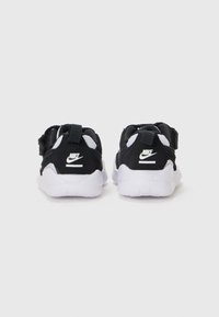 Baskets Nike noires avec des accents blancs, présentant une tige en mesh, un col rembourré et une semelle en caoutchouc texturé. La vue arrière montre un détail du logo.