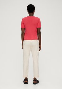 Röd kortärmad tröja med en figursydd design, matchad med ljusbeige byxor och svarta sandaler. Tyget verkar slätt och lättviktigt.