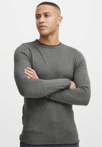 Gray long-sleeve shirt with a round neckline, fitted design, and textured fabric, displayed on a model with crossed arms against a white background.