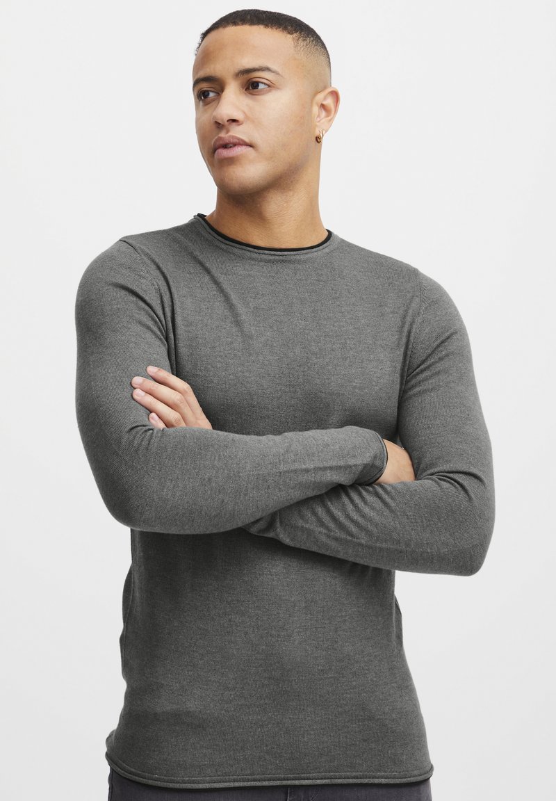 Gray long-sleeve shirt with a round neckline, fitted design, and textured fabric, displayed on a model with crossed arms against a white background.