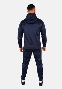Marineblauer Trainingsanzug mit Kapuze, glattem Stoff, taillierter Passform, gerippten Bündchen und Taillenbund, kombiniert mit sportlichen Sneakern.