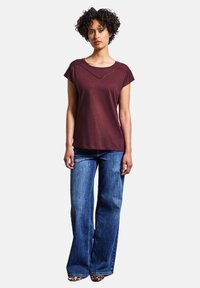 T-shirt court bordeaux à encolure dégagée et détails cousus, associé à un jean bleu à jambes larges. La tenue est accompagnée de chaussures à motif animal.