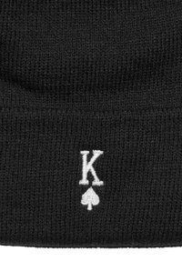 Svart stickad mössa med en vit broderad "K" och spadedesign. Materialet är texturerat och mjukt, med en åtsittande passform.