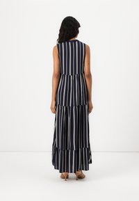 Vestido maxi riscado em azul-marinho com design sem mangas, bainha em camadas e riscas verticais brancas. Tecido suave, comprimento até o tornozelo, com uma silhueta fluida.