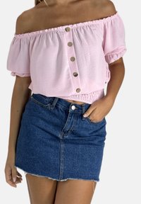 Lyserød skulderfri top med elastisk talje og knappedetalje, kombineret med et tætsiddende denimskørt med frynset kant.