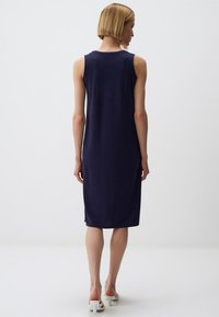 Granatowa sukienka bez rękawów z miękkiego, gładkiego materiału, do kolan, o luźnym kroju, z prostym okrągłym dekoltem i minimalną ilością detali.