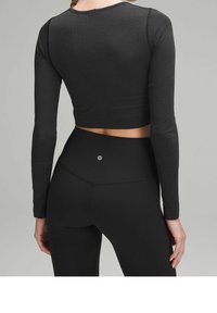 Schwarzes, geripptes, langärmliges Croptop, kombiniert mit hoch taillierten schwarzen Leggings, die ein kleines Logo auf der Rückseite haben. Glattes, eng anliegendes Material.