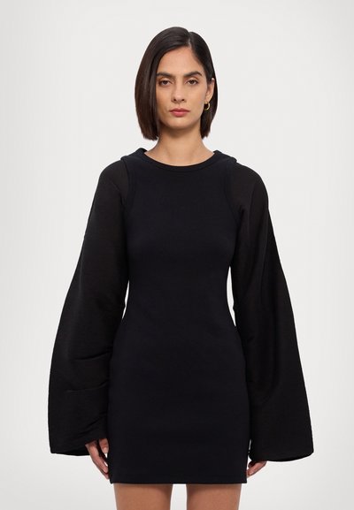 Musta mekko, jossa on pitkät, leveät hihat. Valmistettu ribbausmateriaaleista, joissa on sileä pinta. Ominaisuuksiin kuuluu pyöreä pääntie ja tiukka siluetti.