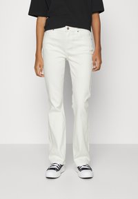 Jeans de pierna recta blancos hechos de denim, con un bolsillo delantero, cierre de botón y combinados con zapatillas negras y blancas.