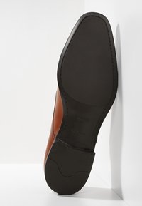 Semelle d'une chaussure habillée en cuir marron avec une semelle extérieure en caoutchouc noir, des coutures détaillées et la marque "BOSS" embossée sur le talon et la zone de la voûte.