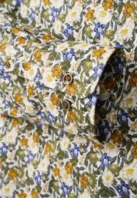 Blusenhemd mit floralem Muster, das einen weißen Hintergrund mit gelben, orangefarbenen und blauen Blumen sowie grünen Blättern zeigt; detaillierte braune Knöpfe betonen die Manschetten.