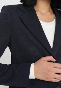 Blazer navy de tejido texturizado con un diseño estructurado, que presenta solapas con muesca, cierre de un solo botón y detalles de costura sutiles.