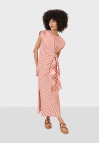 Maxikleid mit rot-weißen Streifen, asymmetrischem Ausschnitt und gebundenem Taillendetail. Das Model trägt braune Plateausandalen.