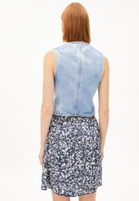 Denimweste in Hellblau mit verkürztem Schnitt, kombiniert mit einem knielangen Blumenrock in Marineblau und Weiß, der einen gerafften Bund hat.