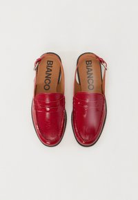 Scarpe slip-on in pelle rossa con una finitura lucida, dotate di tacco basso, dettagli cuciti e una cinghia regolabile sul lato.