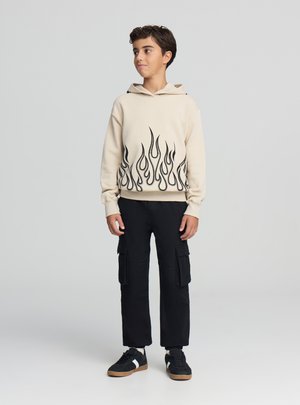 Felpa con cappuccio beige con motivo a fiamme nere all'orlo, abbinata a pantaloni cargo neri e sneaker nere con dettagli bianchi. Tessuto liscio, vestibilità casual.