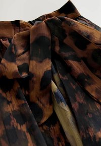 Tissu imprimé mettant en avant des tons chauds de marron, noir et or avec une surface douce et texturée. Comprend un détail de taille nouée très visible.