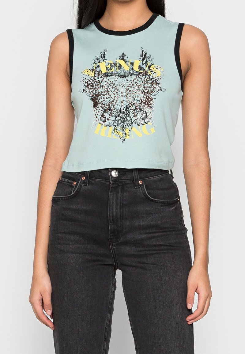 Ärmlös ljusblå crop top med svart kant, utsmyckad med en intrikat blommönster och vingad design samt gul text, matchad med högmidjade svarta jeans.