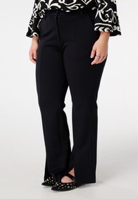 Zwarte, op maat gemaakte broek met een rechte pasvorm, voorzien van een gladde textuur, voorplooien en zijslitten aan de zoom, gecombineerd met zwart gespen schoenwerk.