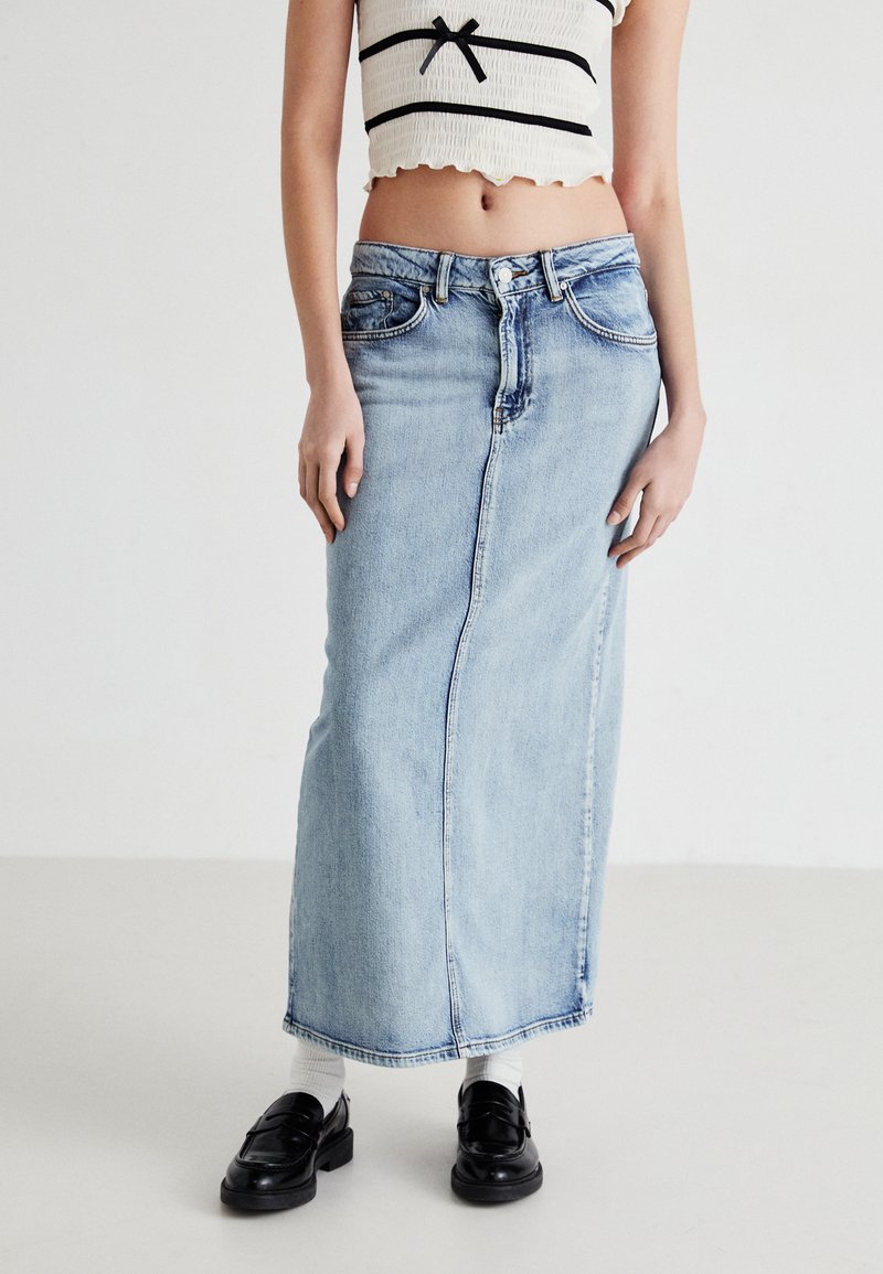 Light blue denim skirt, knee-length with a straight cut. Features belt loops, front pockets, stitched seams, and a raw hem. Worn with black loafers.