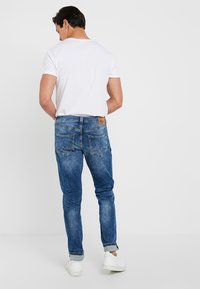 Wygodne, wyblakłe niebieskie dżinsy o dopasowanym kroju, z pięcioma kieszeniami i jasnymi przeszyciami. Noszone z gładką białą koszulką i białymi trampkami.