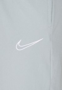Hellgraue Sporthose aus glattem Stoff; verfügt über ein weißes, gesticktes Nike-Logo auf der linken Seite. Einfaches und schlankes Design.