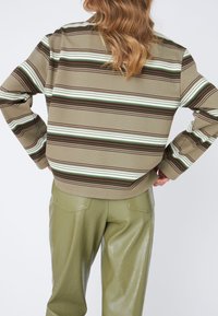 Pull rayé aux tons marron, vert et blanc, en tissu texturé ; assorti à un pantalon brillant vert olive.