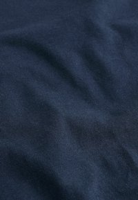 Námornícka modrá bavlnená tkanina s ryhovanou textúrou, ktorá zobrazuje hladké záhyby a jemný lesk. Materiál je ľahký a flexibilný.