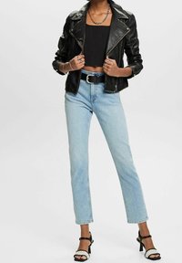 Veste de motard en cuir noir, top noir court, jean bleu clair droit, et sandales à talons noires avec double sangle à la cheville.