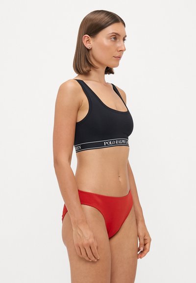 Black sports bra with a logo band, paired with red bikini briefs. Smooth fabric and fitted design, showcasing a simple and clean aesthetic.