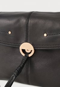 Μαύρο δερμάτινο τσαντάκι χειρός με χρυσό κυκλικό κούμπωμα και πλεγμένη δερμάτινη λεπτομέρεια λουριού σε απλό λευκό φόντο.